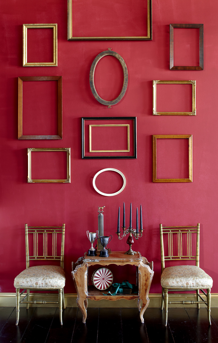 Empty frames on red wall with dining chairs.